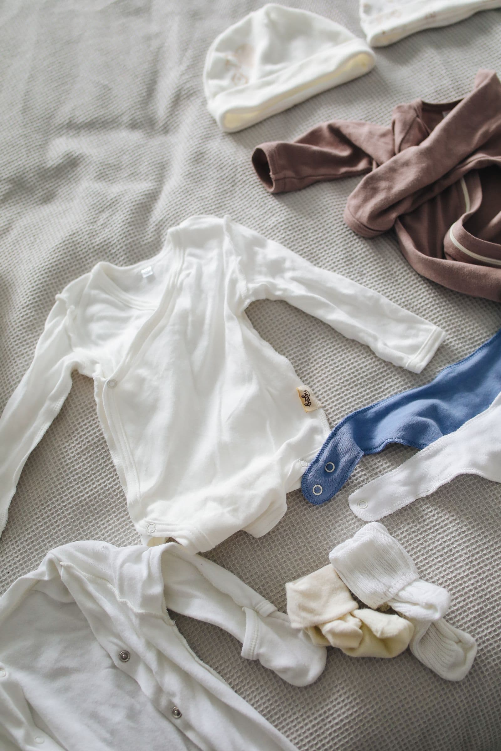Newborn onesie, beanie, and soft baby clothes arranged on a waffle-knit blanket