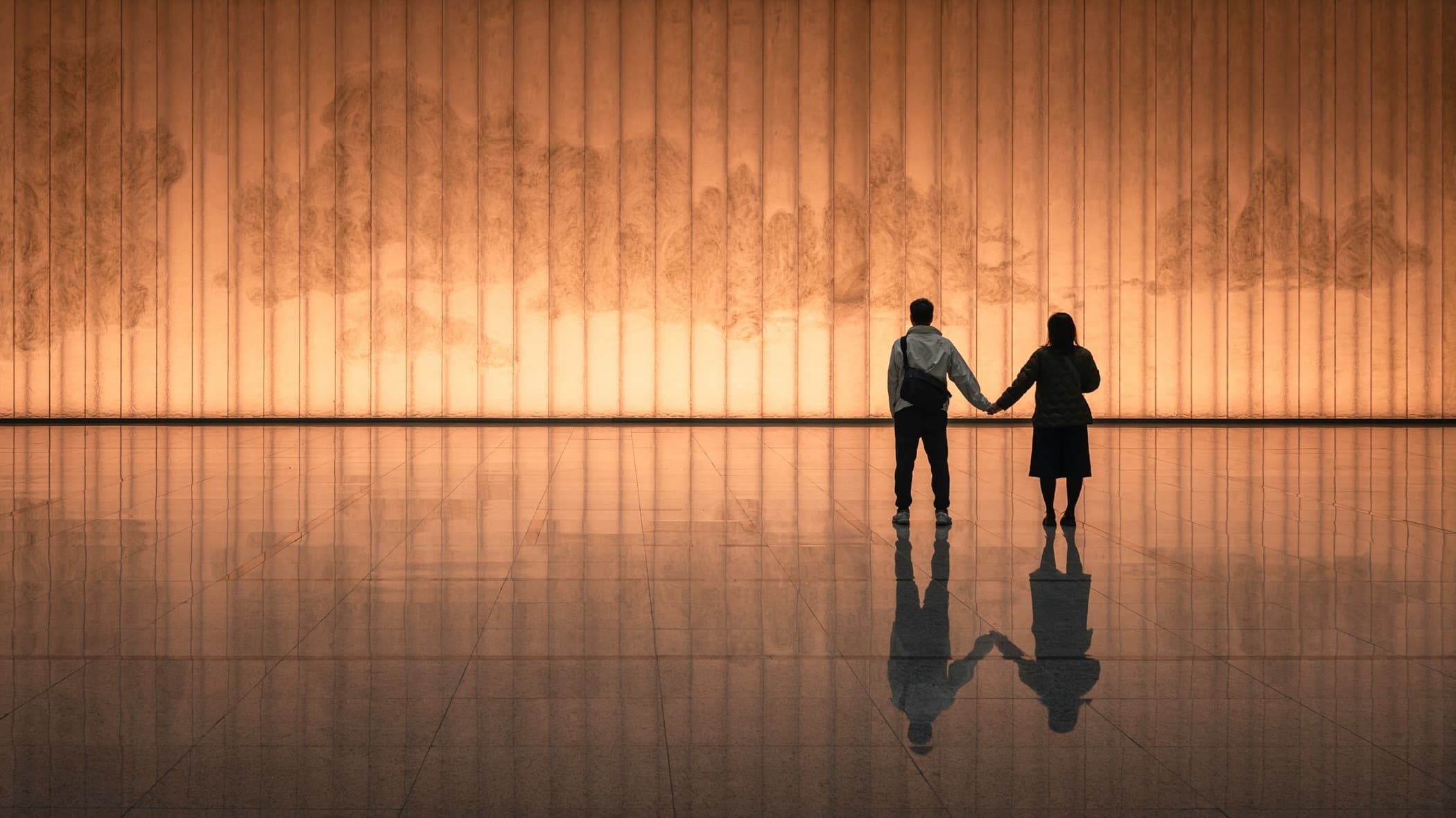 A couple holding hands, seen from behind, in front of a glowing wall in Shanghai