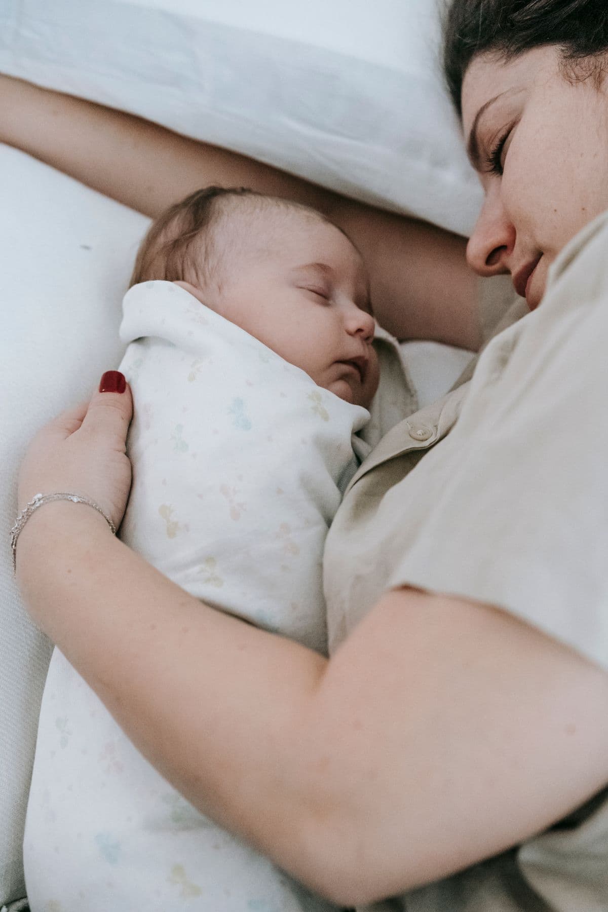 Mother sleeping beside her swaddled newborn at home