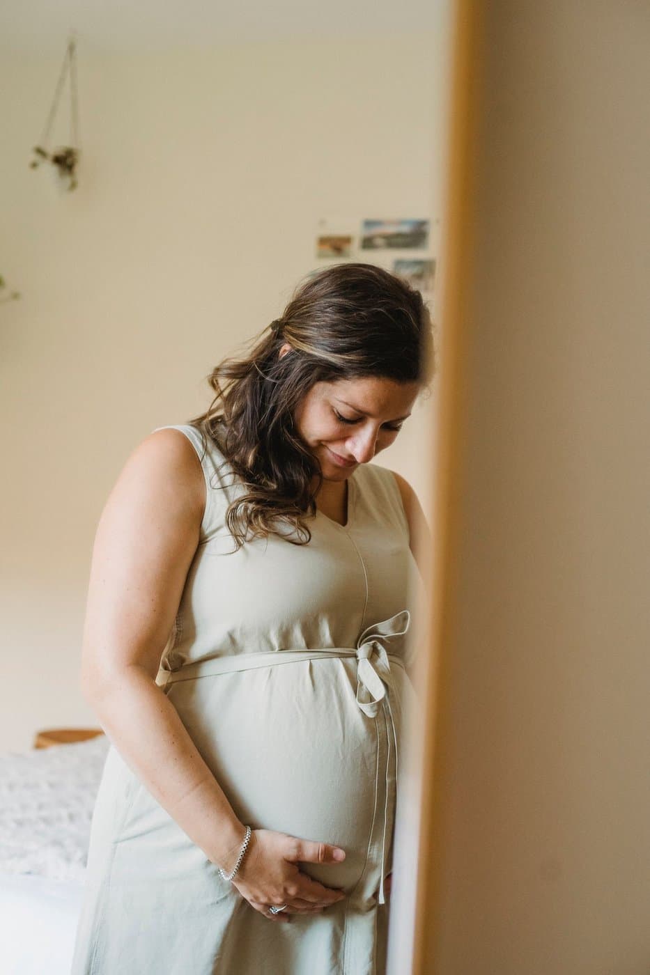 Expecting parent cradling her belly in a softly lit bedroom